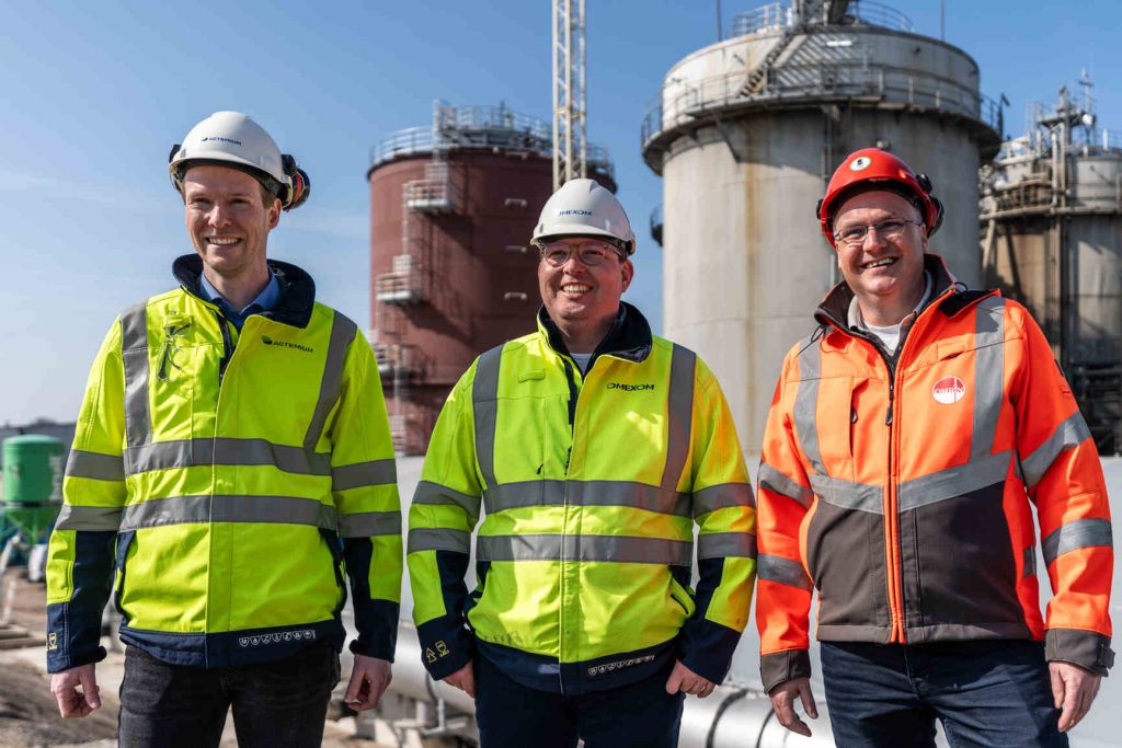 Drie mannen in veiligheidsvesten staan voor de vergisterinstallaties op de locatie van Omrin.